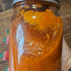 May include: A glass jar filled with a bright orange sauce. The jar has a silver lid and is partially filled with the sauce.