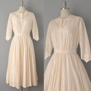 May include: A white eyelet dress with a peter pan collar and 3/4 sleeves. The dress has a fitted bodice and a full skirt.