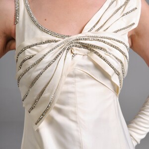 May include: A white sleeveless dress with a rhinestone embellished neckline and bodice. The dress has a fitted bodice and a flowing skirt.