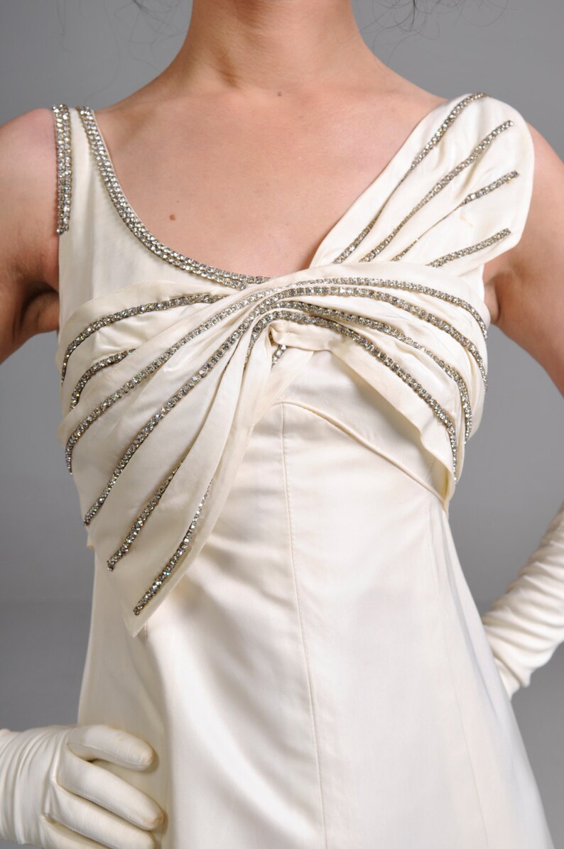 May include: A white sleeveless dress with a rhinestone embellished neckline and bodice. The dress has a fitted bodice and a flowing skirt.
