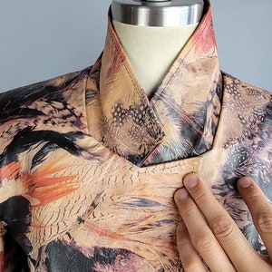 May include: A brown leather jacket with a colorful feather print. The jacket has a mandarin collar and a zipper closure.
