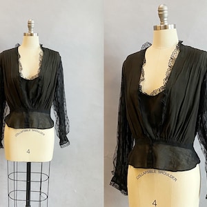 May include: A black sheer blouse with lace detailing on the sleeves and neckline. The blouse has a fitted bodice and a slightly flared hem. The text "COLLAPSIBLE SHOULDER" is printed on the mannequin.