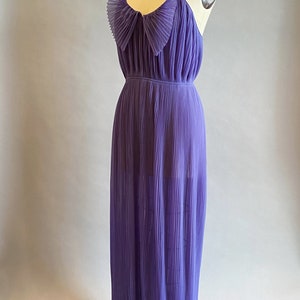 May include: A long, purple, pleated dress with a bow at the neckline. The dress is sleeveless and has a flowy, feminine silhouette.