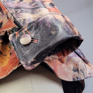 May include: A close-up of a black leather jacket with a colorful floral print. The jacket has a button closure and a fold-over cuff. The print features a variety of flowers and leaves in shades of pink, yellow, and orange.