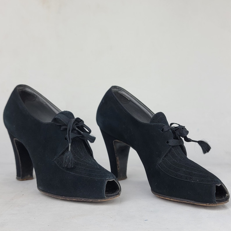 K&ouml;nnte beinhalten: Ein Paar schwarze Wildlederschuhe mit Peeptoe, Schn&uuml;rung vorne und Quastenverzierung.