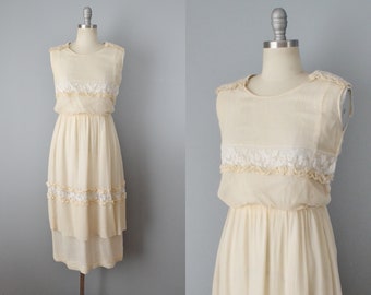 May include: A sleeveless, ivory-coloured dress with a tiered skirt and lace trim. The dress is made of a lightweight fabric and has a relaxed fit.