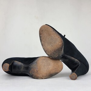 K&ouml;nnte beinhalten: Ein Paar schwarze Wildlederschuhe mit Absatz und spitzer Zehenpartie. Die Schuhe sind von unten zu sehen, wodurch die Sohlen sichtbar werden.