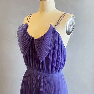 May include: A purple pleated maxi dress with a ruffled neckline and thin straps.