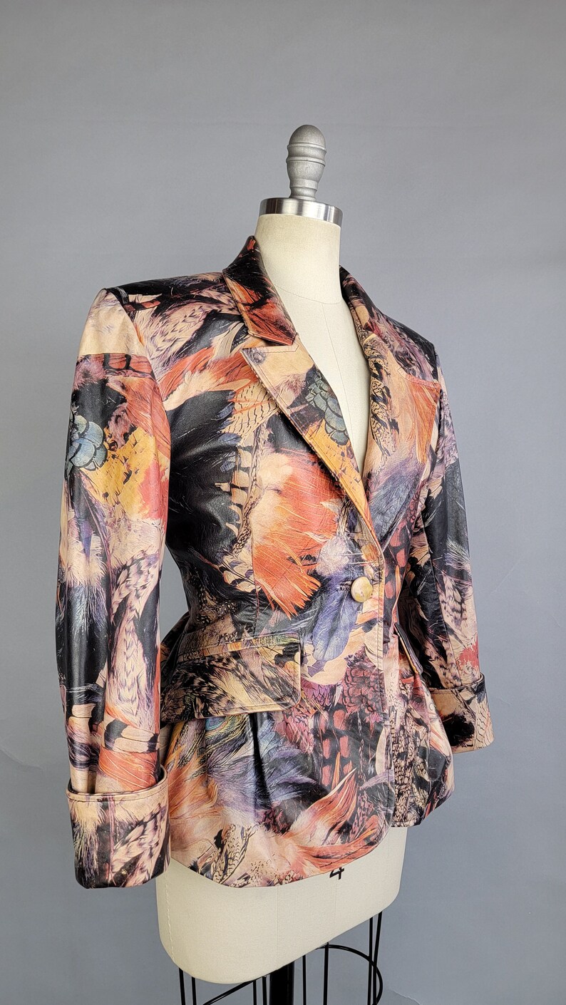 May include: A fitted blazer with a colorful feather print. The blazer has a single button closure and long sleeves with a cuffed hem.