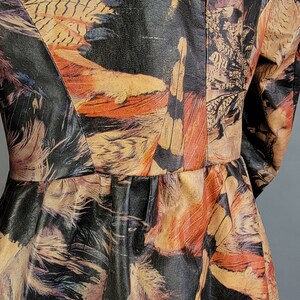 May include: A black leather jacket with a colorful feather print. The jacket has a fitted silhouette and a ruffled hem.