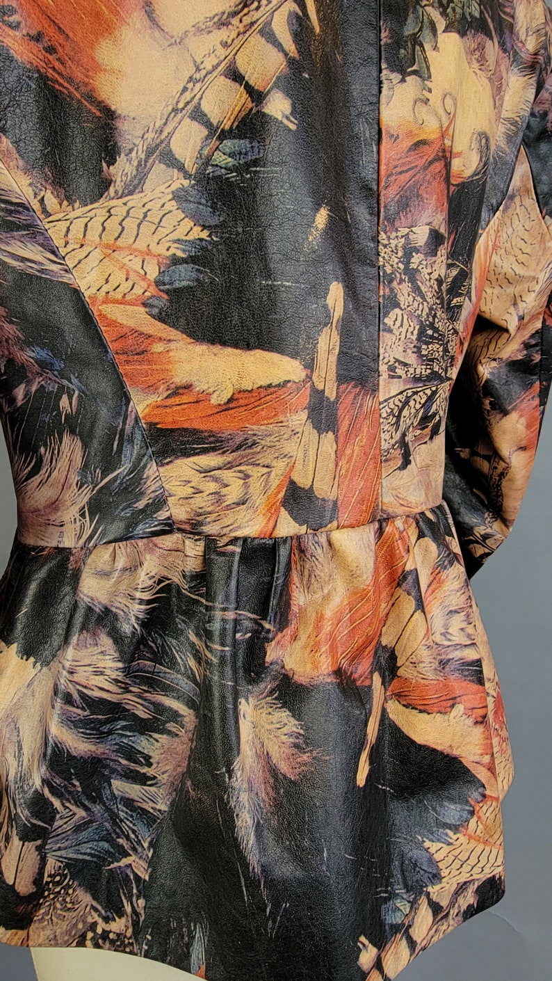 May include: A black leather jacket with a colorful feather print. The jacket has a fitted silhouette and a ruffled hem.