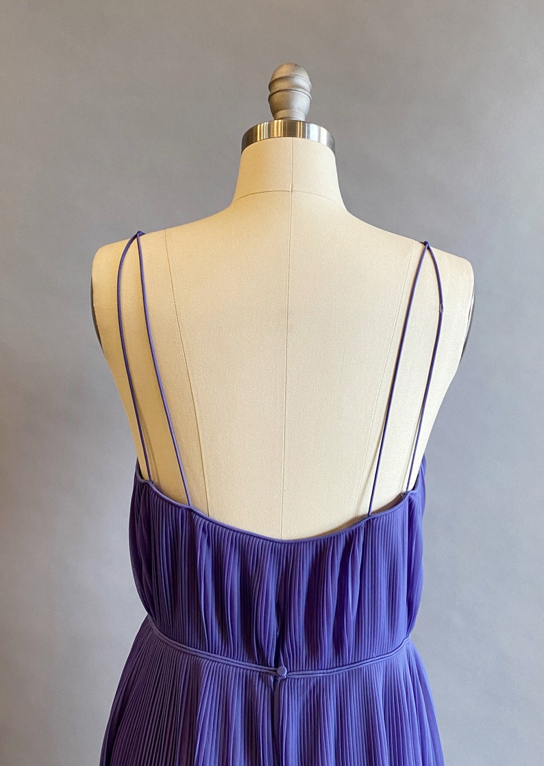 May include: A purple pleated sleeveless dress with thin straps. The dress has a fitted bodice and a flowing skirt.