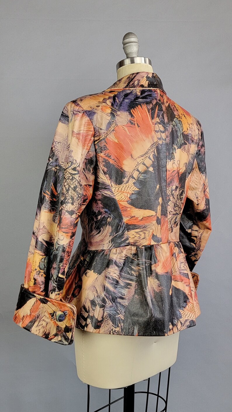 May include: A brown leather jacket with a colorful feather print. The jacket has a fitted waist and long sleeves with cuffed ends.