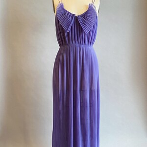 May include: A long, purple, pleated maxi dress with thin straps and a ruffled neckline. The dress is on a white mannequin against a light gray background.