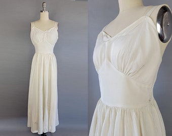 May include: Ivory-colored vintage dress with a sweetheart neckline and spaghetti straps. The bodice is gathered, and the skirt flows to the floor. The dress is displayed on a mannequin against a gray background.