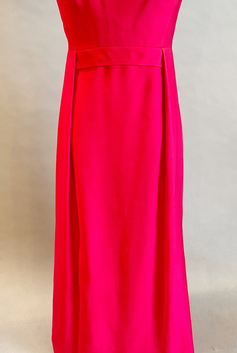 May include: A long, sleeveless, bright pink dress with a simple design and a narrow belt at the waist.