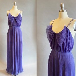 May include: A long, purple, pleated dress with a ruffled neckline and thin straps. The dress is made of a sheer fabric and has a flowing silhouette.
