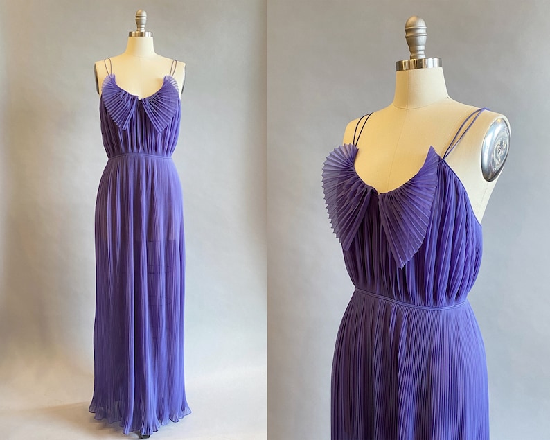 May include: A long, purple, pleated dress with a ruffled neckline and thin straps. The dress is made of a sheer fabric and has a flowing silhouette.