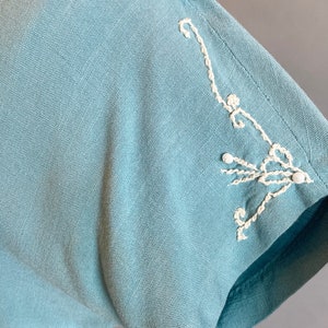 May include: A light blue linen dress with white embroidered details on the sleeve.