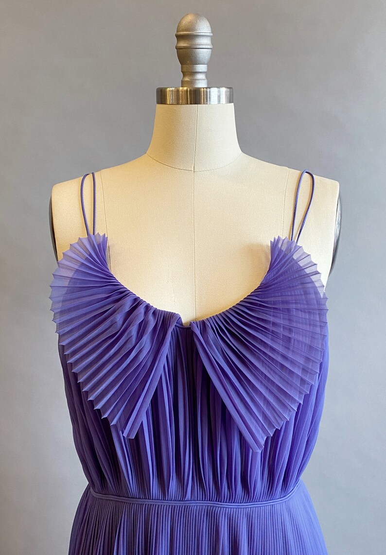 May include: A purple pleated sleeveless dress with a ruffled neckline. The dress is made of a sheer fabric and has a fitted bodice.