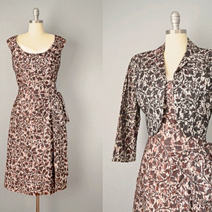 May include: A brown and white patterned dress with a matching cropped jacket. The dress has a scoop neck and a tie at the waist. The jacket has a collar and three-quarter sleeves.