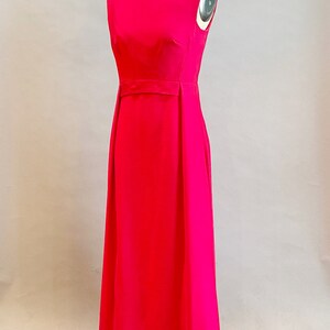 May include: A sleeveless, floor-length, bright pink dress with a simple, elegant design. The dress has a fitted bodice and a flowing skirt.