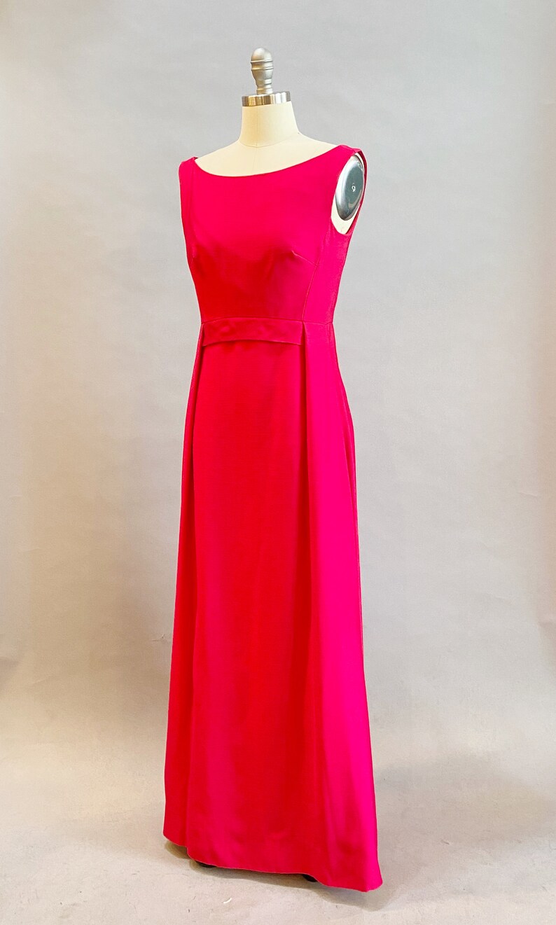 May include: A sleeveless, floor-length, bright pink dress with a simple, elegant design. The dress has a fitted bodice and a flowing skirt.