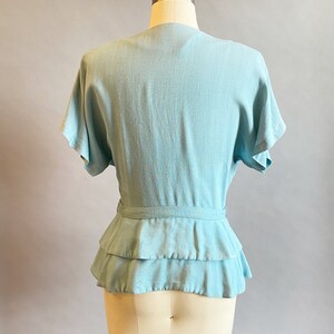 May include: A light blue blouse with a ruffled hem and a tie at the waist.