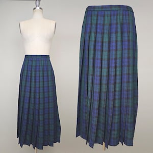 May include: A long, pleated skirt in a blue, green, and black plaid pattern. The skirt is displayed on a mannequin and also shown separately. The fabric has a classic, woven texture. The skirt's design is a timeless style.
