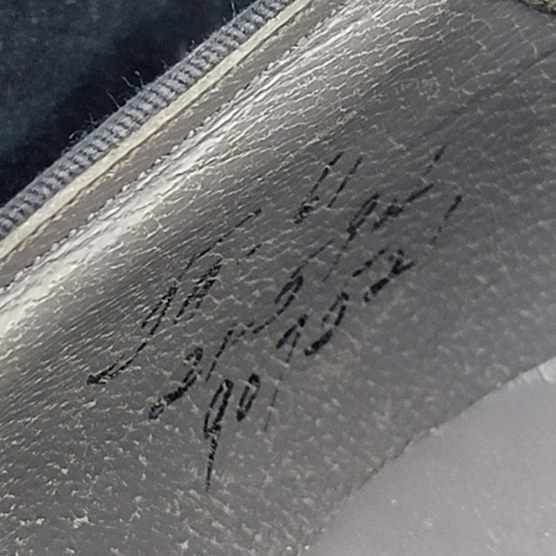 K&ouml;nnte beinhalten: Nahaufnahme einer grauen, strukturierten Oberfl&auml;che mit handschriftlichem Text, der "Made in Italy 901 1932" lautet.
