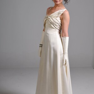 May include: A woman wearing a white satin gown with beaded embellishments and long white gloves. She is wearing silver heels and has her hair styled with a flower.