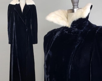 May include: A long black velvet coat with a white fur collar. The coat has a long, flowing silhouette and a classic design.