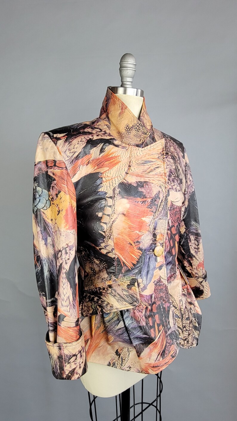 May include: A short-sleeved, multi-colored jacket with a feather print. The jacket has a high collar and a button closure. The jacket is made of a soft, supple leather.