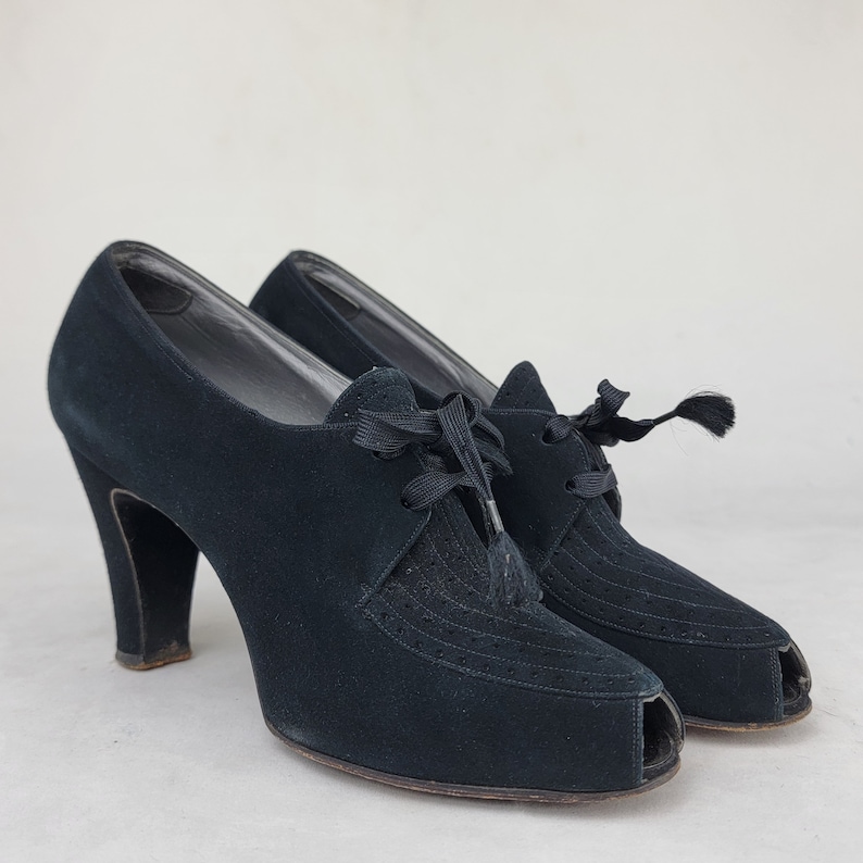K&ouml;nnte beinhalten: Ein Paar schwarze Wildlederschuhe mit Peeptoe, Schn&uuml;rung und Quaste.