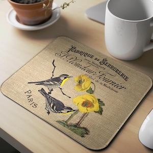 May include: A beige mousepad with a vintage design featuring two birds perched on branches with yellow flowers. The text "Fabrique de Serrurerie pour Hameçons 10 Rue de la Madeleine Paris" is printed on the mousepad.