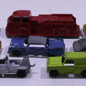 May include: A collection of vintage toy cars in various colors, including red, yellow, blue, green, and gray. The cars are made of metal and have a worn, distressed look. Some of the cars have visible rust and scratches.