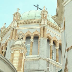 Puede incluir: Un gran edificio blanco y beige con un techo abovedado y una cruz en la parte superior. El edificio tiene ventanas arqueadas y columnas.