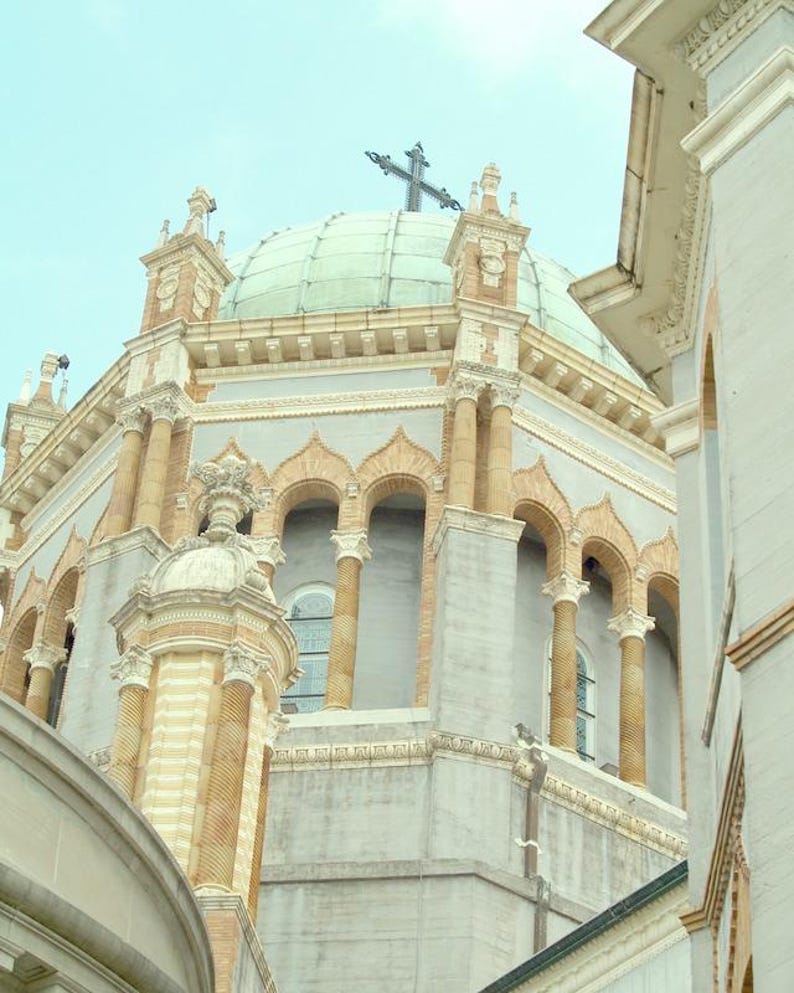 Puede incluir: Un gran edificio blanco y beige con un techo abovedado y una cruz en la parte superior. El edificio tiene ventanas arqueadas y columnas.