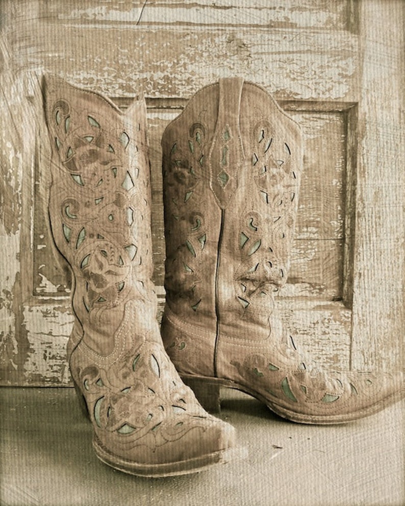Op de afbeelding: Een paar bruine leren cowboylaarzen met ingewikkelde uitgesneden ontwerpen. De laarzen staan tegen een rustieke houten achtergrond.