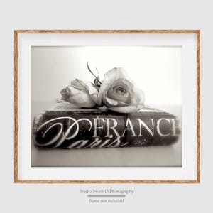 May include: A black and white photograph of a book with the words "France Paris" on the cover. A bouquet of roses is placed on top of the book.