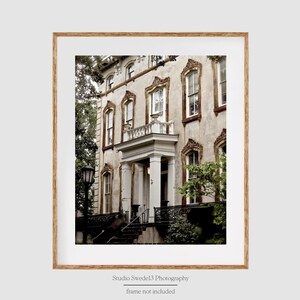 May include: A vintage-style white building with a brown door and a balcony. The building has a faded, weathered look and is surrounded by lush greenery.