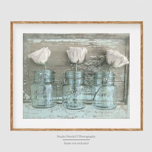 May include: Three white roses in vintage blue glass jars on a weathered light blue wooden background.