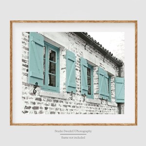 May include: A white brick building with a row of windows with light blue shutters. The shutters are closed and the windows are visible through the slats.