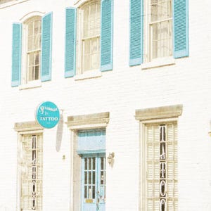 May include: A white building with blue shutters and a blue door. The building has a sign that says "Glamour Ink Tattoo".