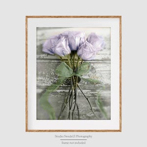 May include: A bouquet of lavender roses with green leaves against a whitewashed wood background.