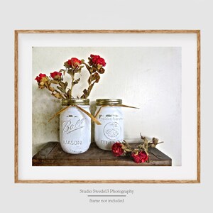 May include: Two white mason jars with red dried roses in them. The jars are on a wooden shelf. The jars are labeled "Ball Mason" and "Golden Harvest".