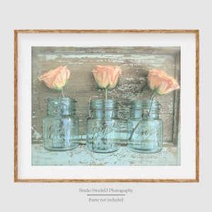 May include: Three peach-colored roses in vintage blue glass jars on a weathered, light blue wooden background.