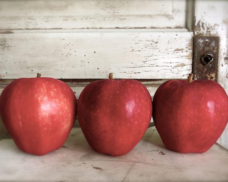 May include: Three red apples on a white wooden surface. The apples are arranged in a row, with the largest apple in the middle.