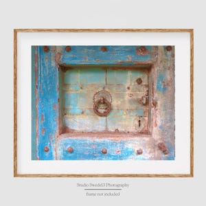 May include: A close-up of a weathered blue wooden door with a rusty metal ring handle and a keyhole. The door is decorated with metal studs and has a faded, layered paint finish.