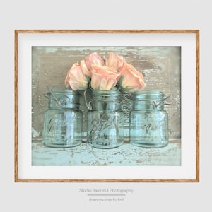 May include: Three vintage blue glass jars with a bouquet of peach-colored roses on a rustic wooden background.